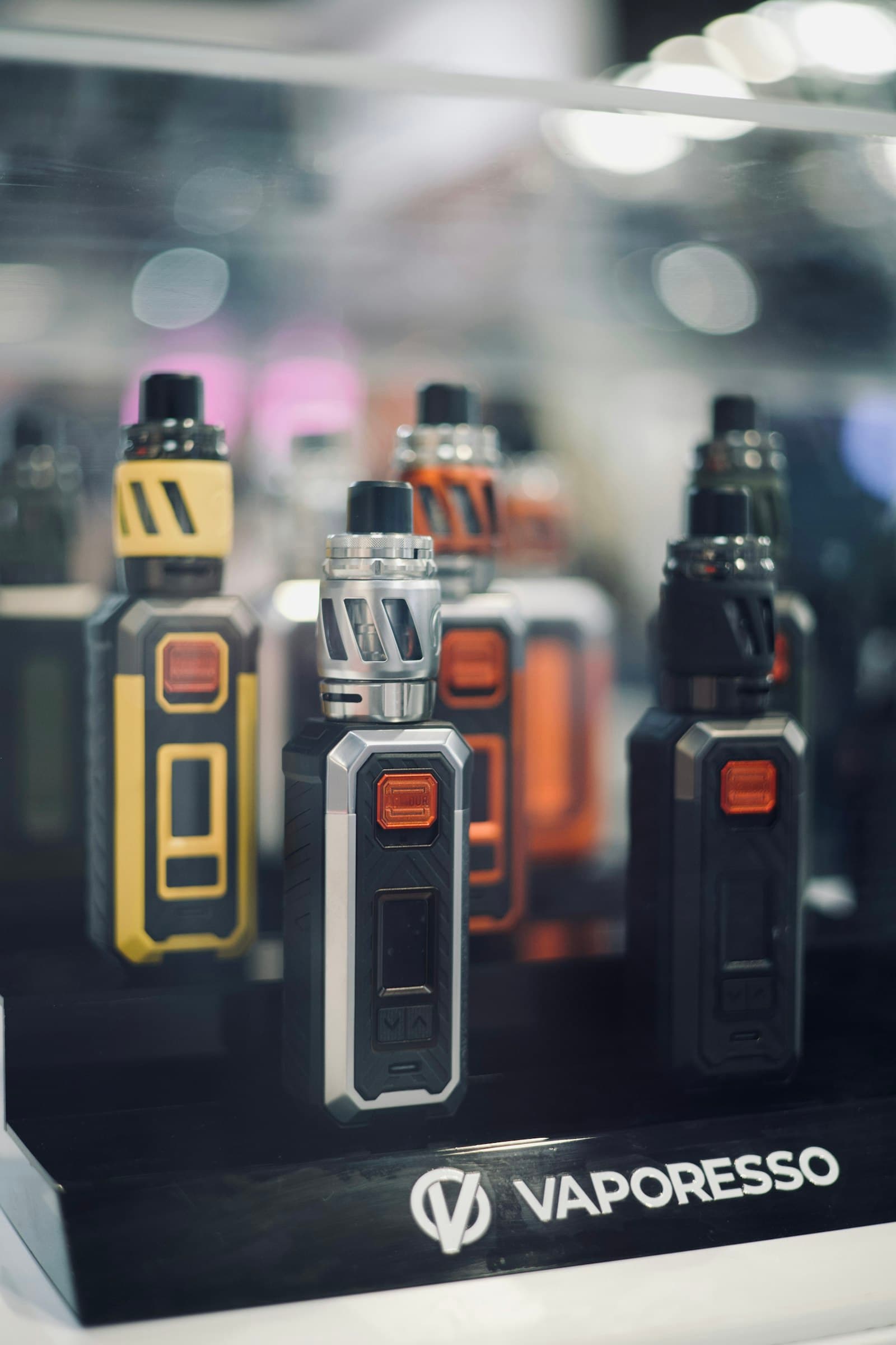 A glass display case in a vape shop showing a row of compact pod mod devices in different colours